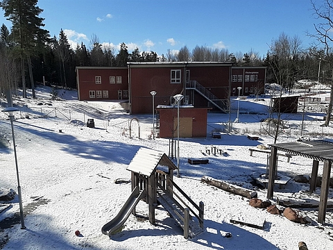 Ein Kindergarten mit Spielplatz auf dem Außengelände. Es ist sonnig, aber überall liegt noch Schnee.
